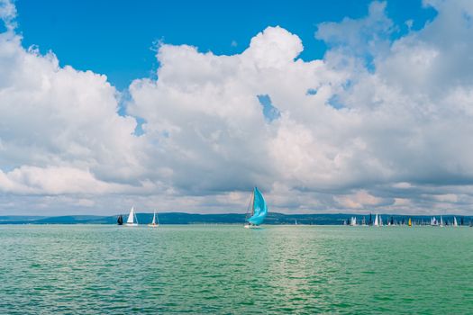 Sailboats gliding on Lake Balaton, Balatonföldvár, Hungary, with puffy clouds and vibrant blue skies.