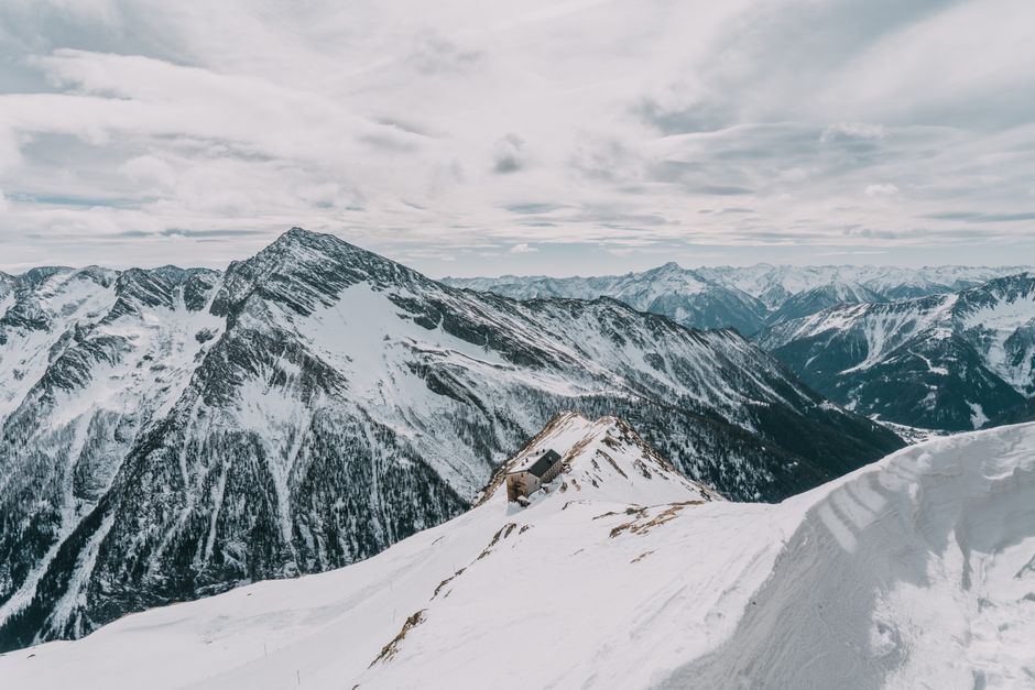 A stark winter scene with snow-covered mountains and a secluded hut.