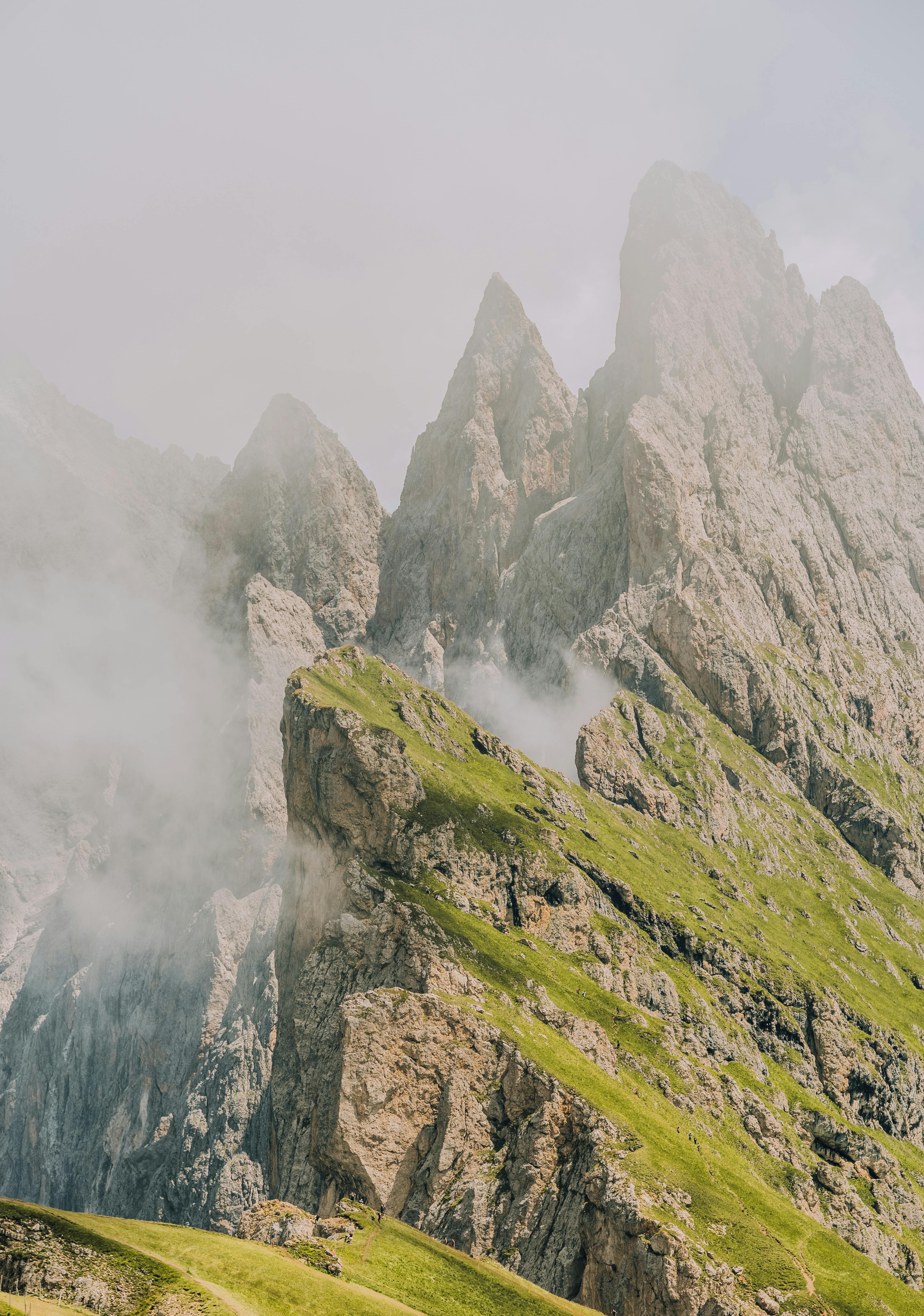 Epic view of sharp rocky peaks with lush greenery and mist, capturing nature's grandeur.