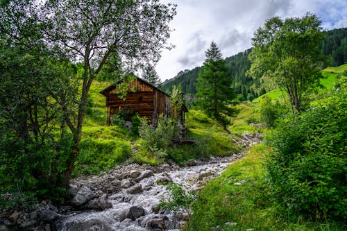 Wooden Cottage beside Stream in Mountain Landscape