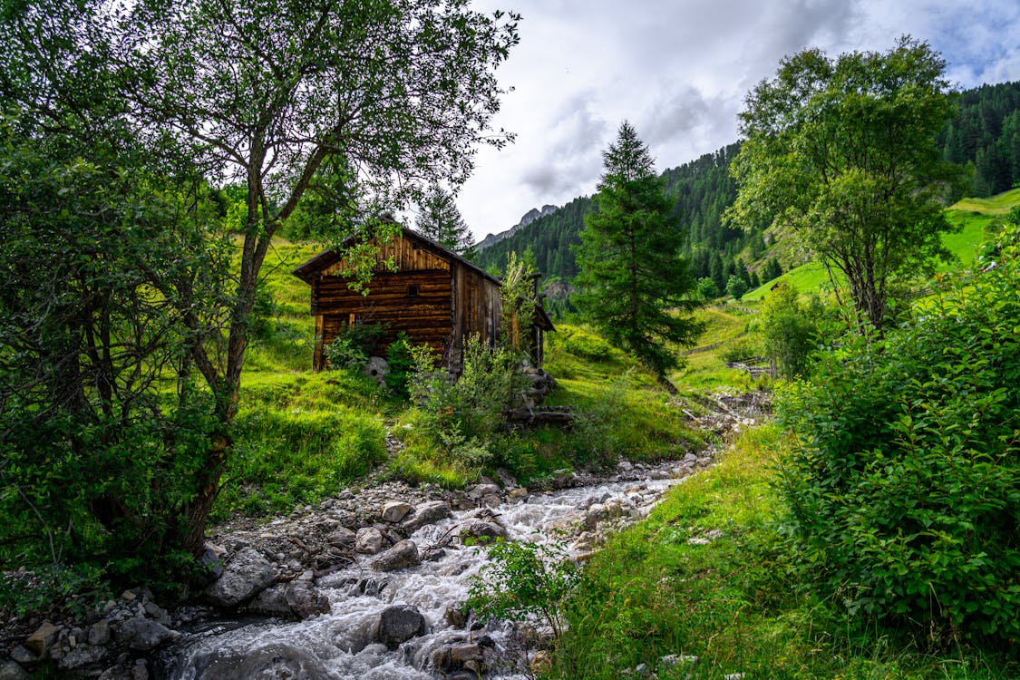 Wooden Cottage beside Stream in Mountain Landscape