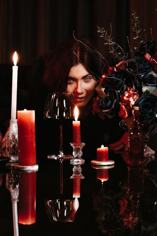 Free A woman in a dark setting with candles, flowers, and reflections evokes a mysterious mood. Stock Photo
