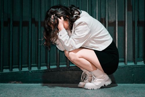 Free Woman crouching with head in hands against city wall, expressing deep contemplation. Stock Photo