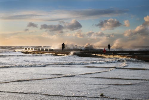 People Standing on a Pier among Waves Breaking on the Shore 