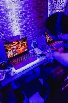 A player deeply engaged in gaming on two laptops in an illuminated room.