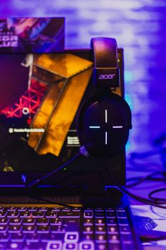 Close-up of a gaming setup featuring an Acer laptop and headset illuminated by colorful lights.