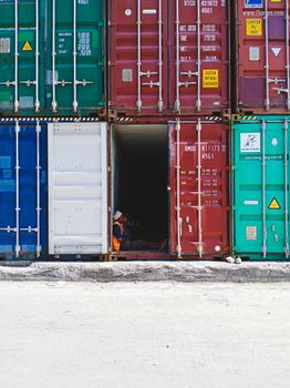 Workers resting inside a shipping container in a stacked shipyard setting.