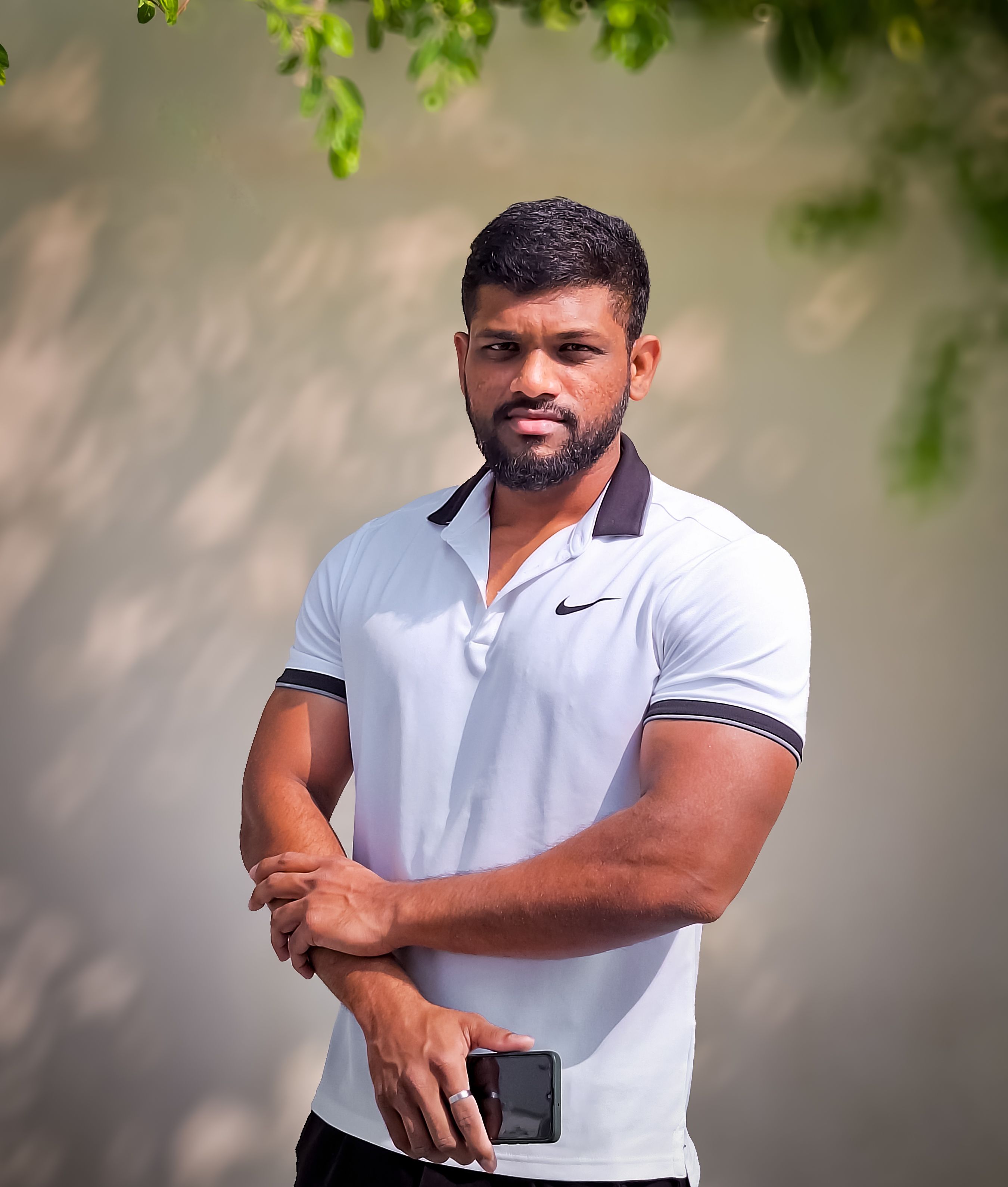 A muscular man standing confidently in a white polo shirt outdoors, showcasing fitness and strength.