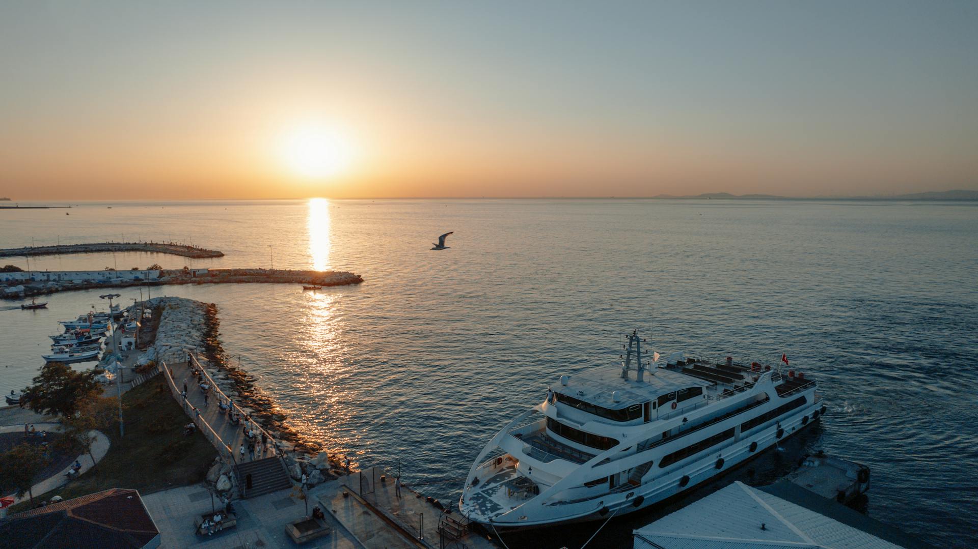 A luxury yacht docked at Yalova harbor as the sun sets, creating a serene coastal scene.
