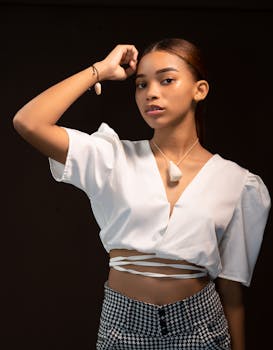 Elegant portrait of a young woman in a stylish white top with jewelry, set against a dark background.