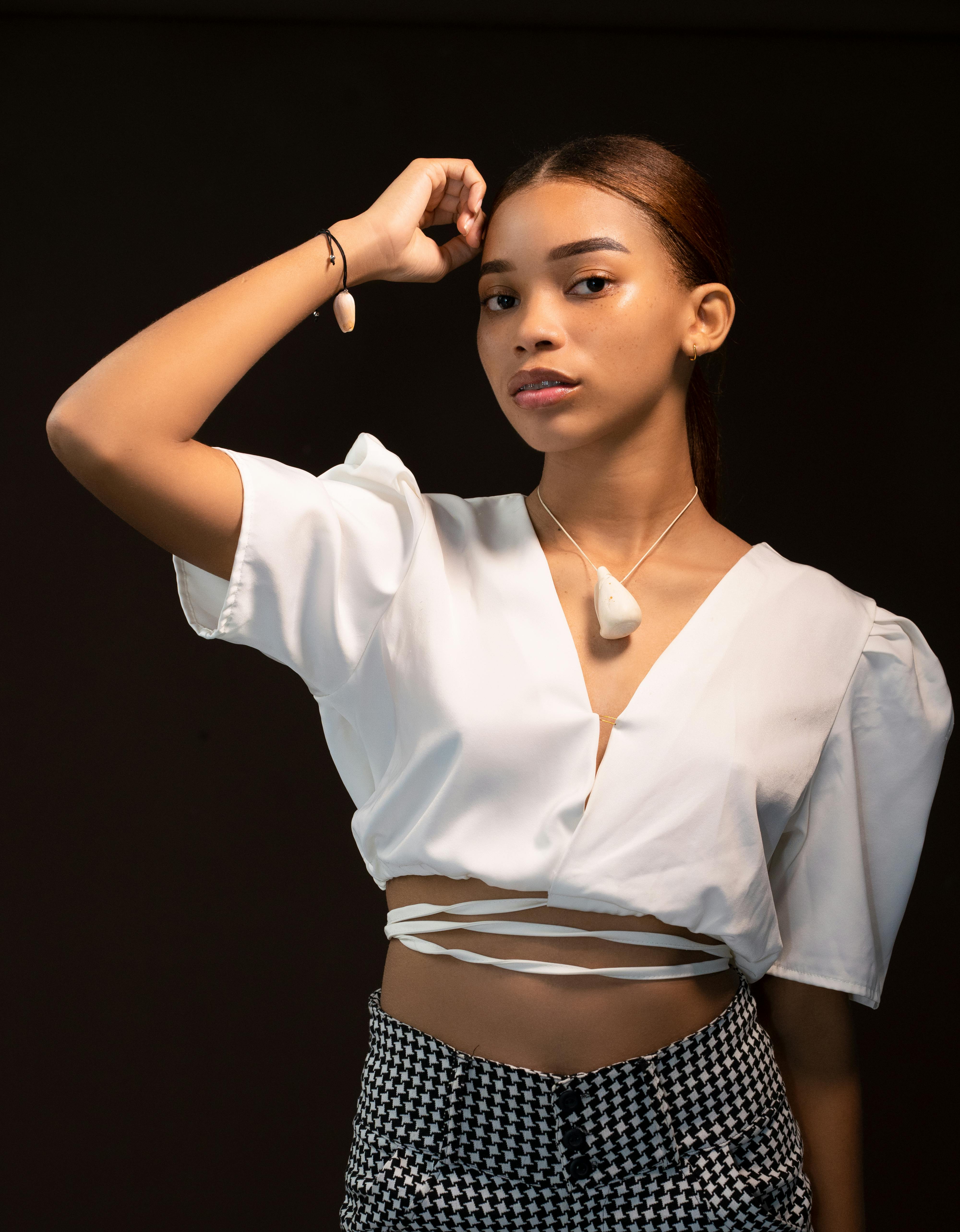 Free Elegant portrait of a young woman in a stylish white top with jewelry, set against a dark background. Stock Photo
