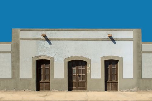 Free A symmetrical facade with three wooden doors under a clear blue sky. Stock Photo