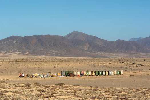 A row of recycling bins and waste in a desert landscape with mountains in the background.