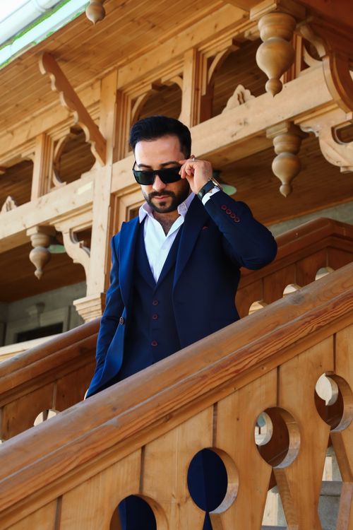 Free Elegant man in a blue suit and sunglasses descending wooden stairs with ornate architecture. Stock Photo