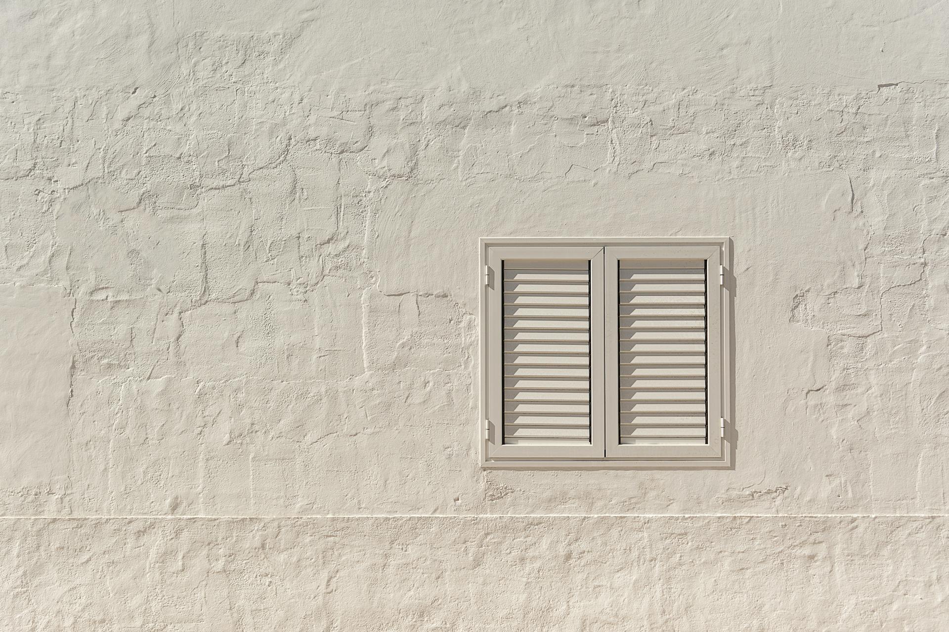 Minimalist image of a white wall adorned with a closed shuttered window.