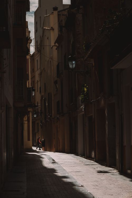 Free A narrow urban alleyway with dramatic sunlight and shadows cast on building facades. Stock Photo