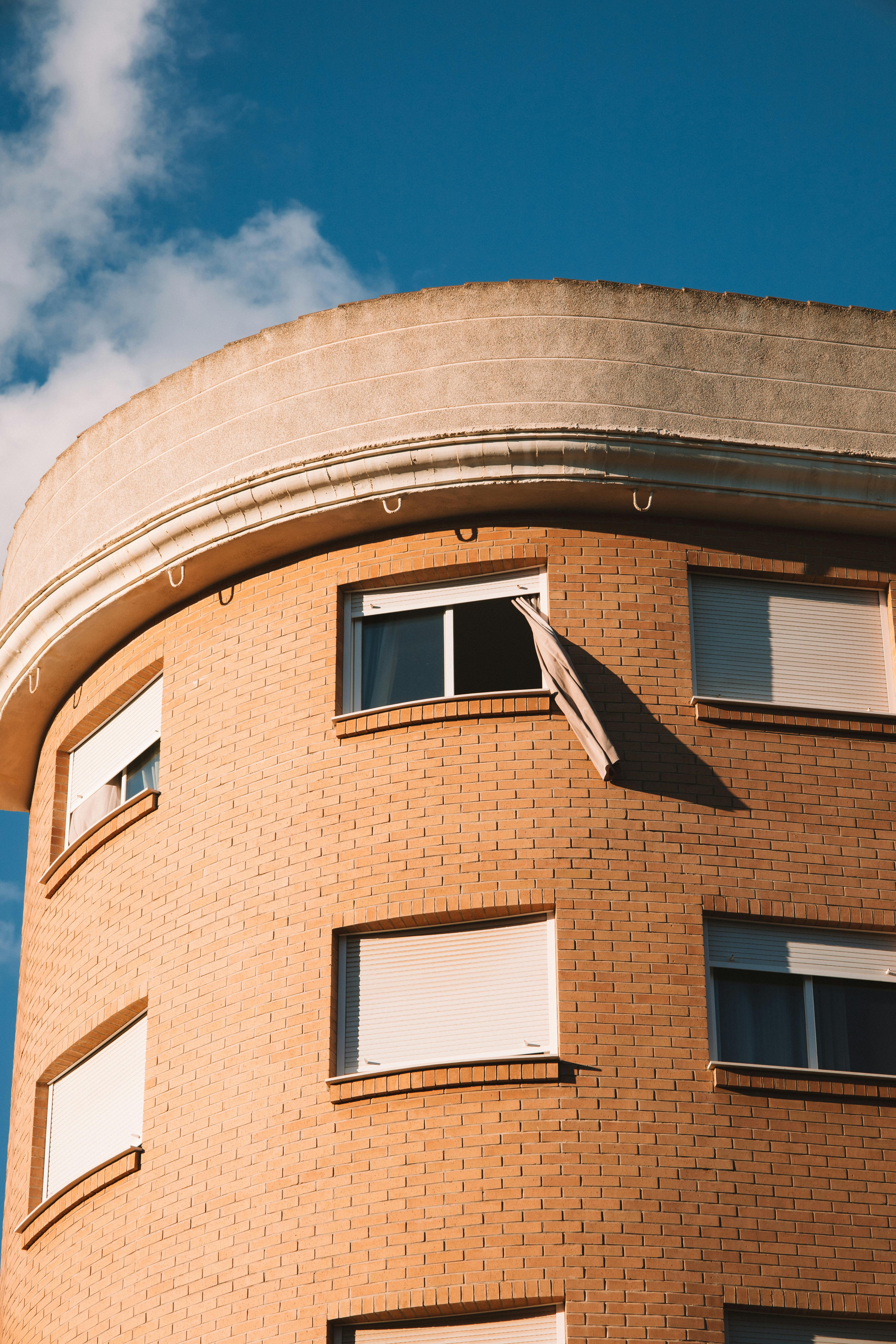 A modern curved building facade with open windows against a clear blue sky.