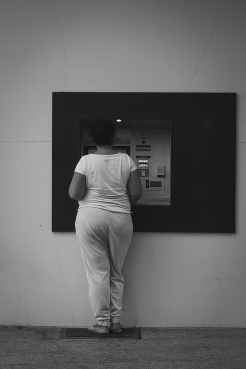 Free Back view of a woman standing at an ATM, captured in a monochrome setting. Stock Photo