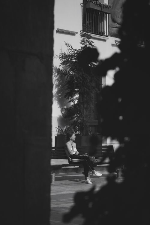 Free A young woman sits quietly on a city bench, captured in black and white. Stock Photo
