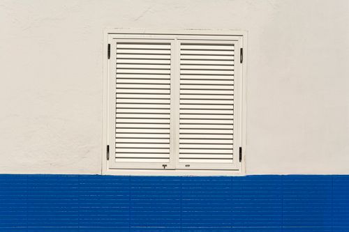 Free Minimalist image of a white shuttered window on a blue wall with clean lines and contrasting colors. Stock Photo