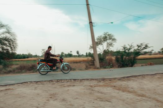 A man rides a motorcycle through the countryside on a sunny day.