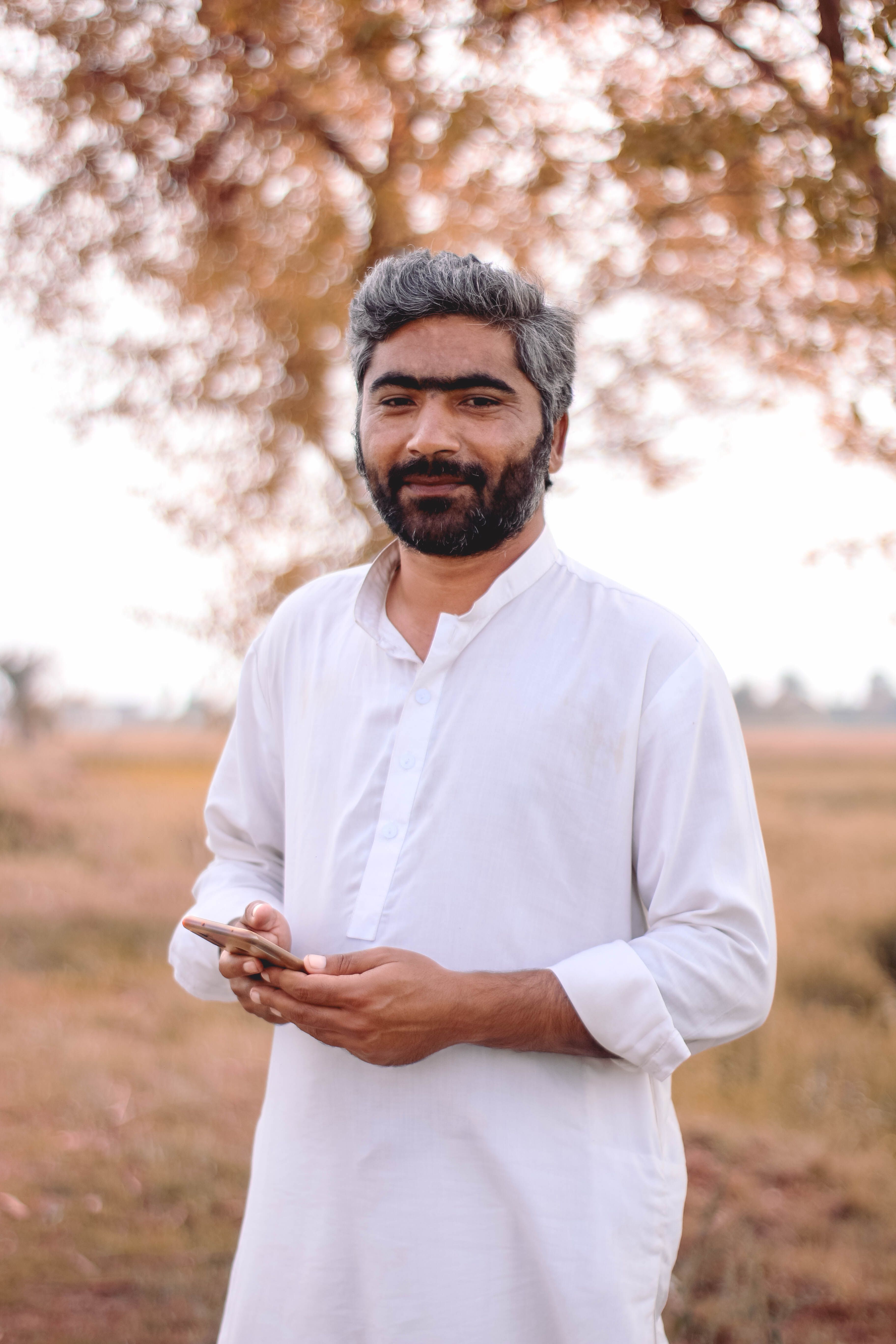 Smiling man in white shirt outdoors during autumn. Natural setting with warm tones.