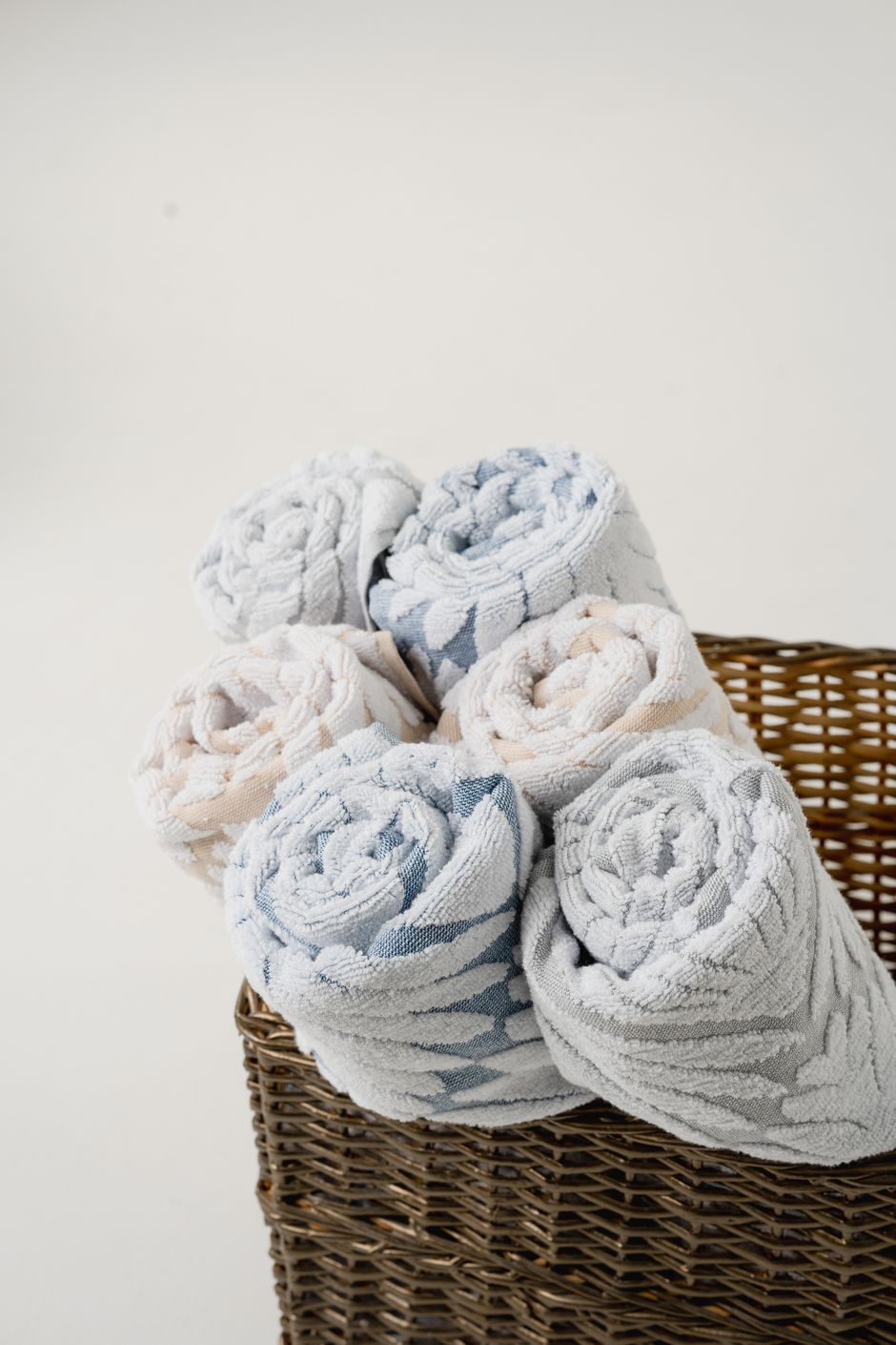 Rolled towels in a wicker basket on a light background, perfect for spa settings.