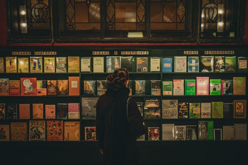Free A woman selecting books from a well-lit shelf in a Saint Petersburg library. Stock Photo