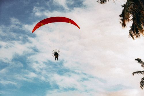 Free A person paragliding with a paramotor beneath a wide blue sky and palm trees, capturing a sense of freedom. Stock Photo