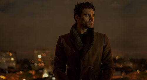 Free Portrait of a man in a winter coat, standing outdoors at night against a city backdrop. Stock Photo