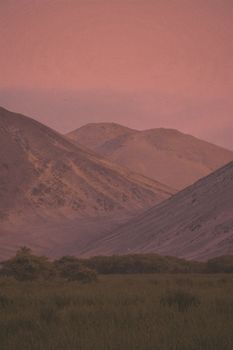 A tranquil evening scene with mist-covered mountains and a pink sky.