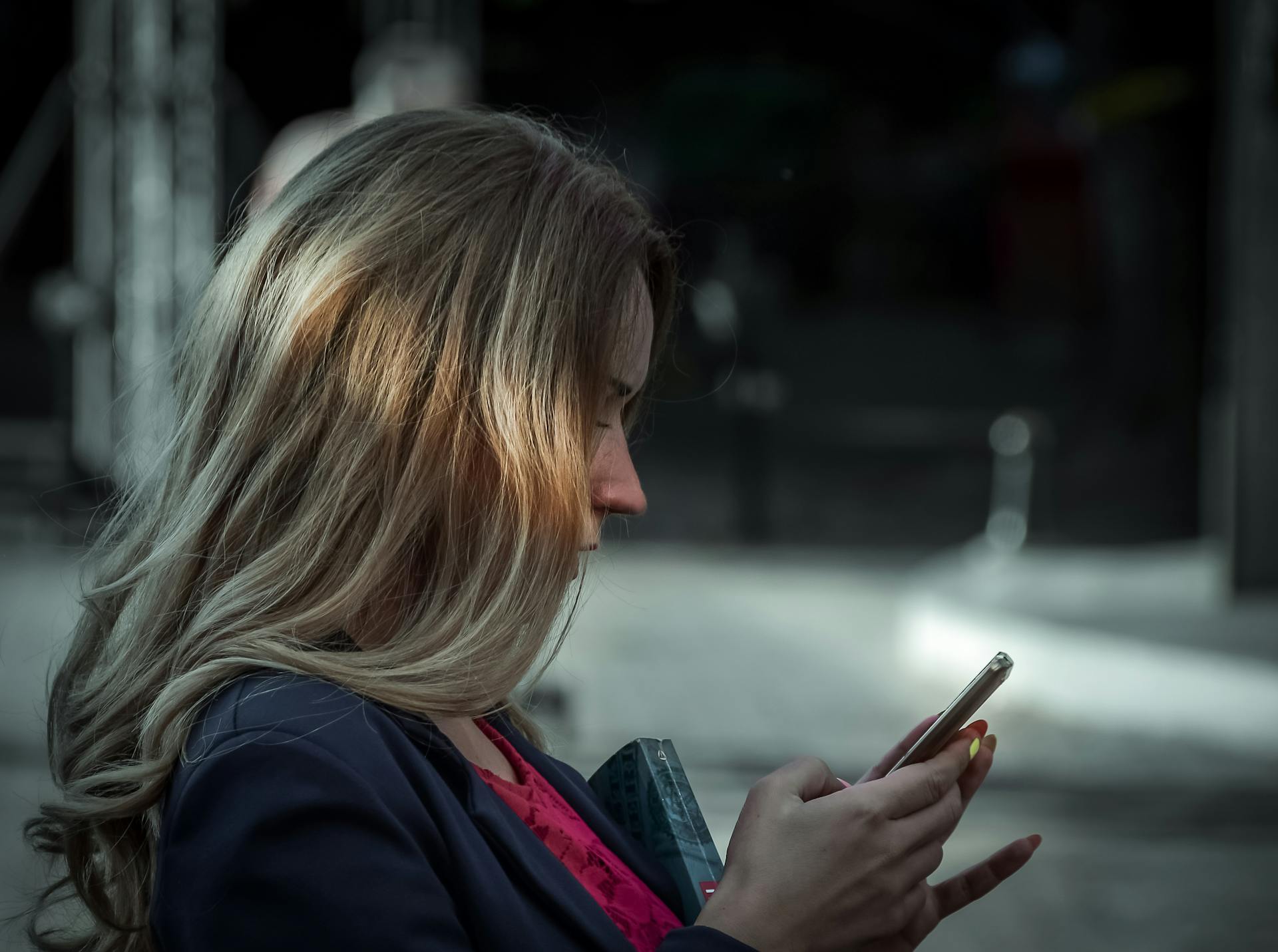 Side profile of a young woman texting on her smartphone in a shaded outdoor area.