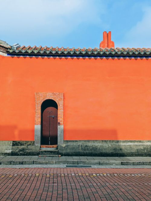 Free Orange wall with a traditional wooden door and tiled roof in an urban setting, offering a colorful and cultural scene. Stock Photo