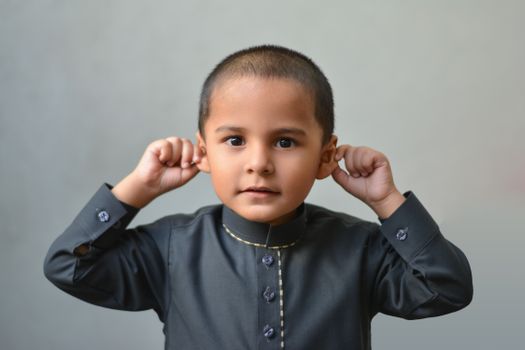 Charming portrait of a young boy in traditional attire playfully posing indoors.