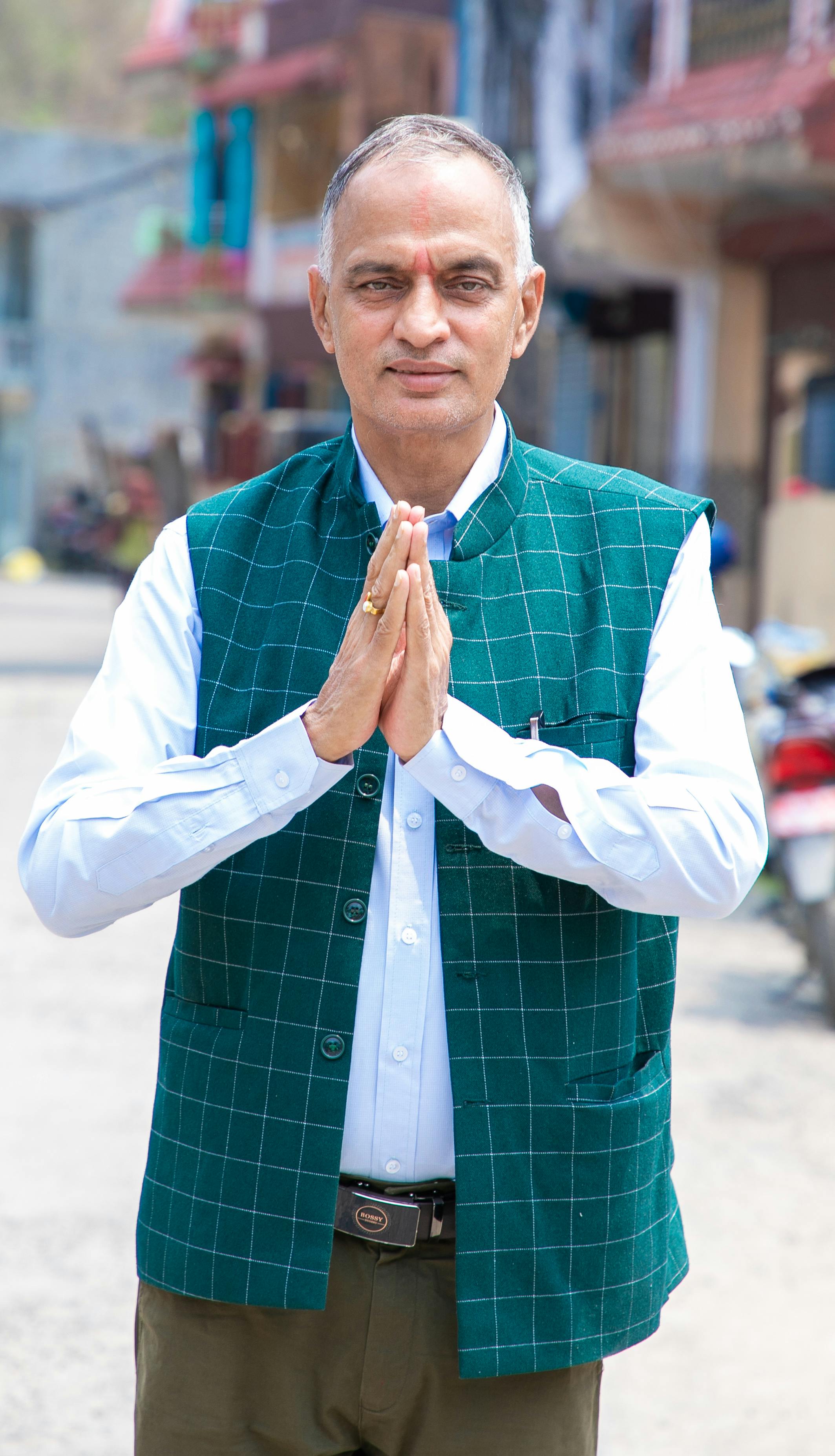 Adult man in green vest doing namaste gesture in an urban setting.