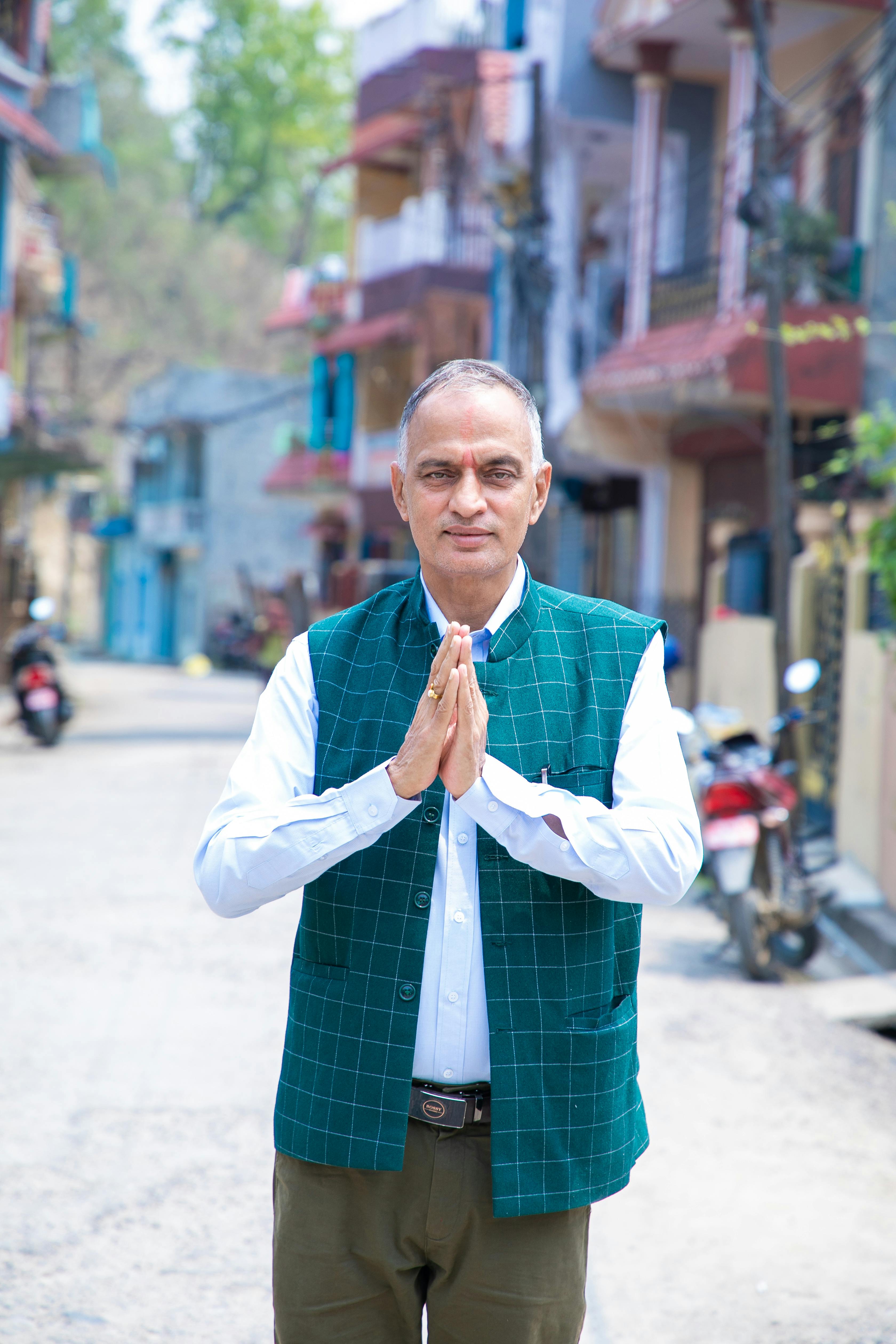 Senior man with folded hands in greeting, standing on a vibrant city street.