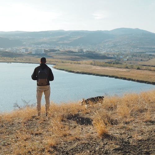 Back View of a Man Standing on a Hill by the Body of Water 