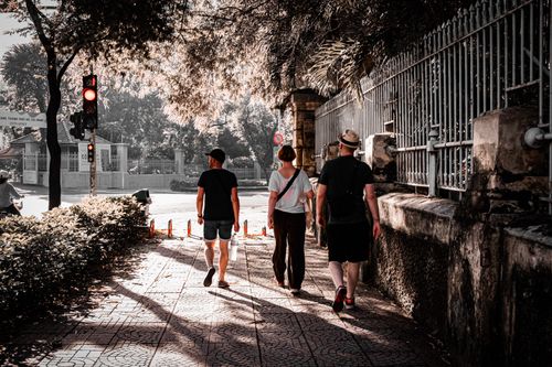 Free Three adults stroll down a shaded urban walkway, illuminated by summer sunlight. Stock Photo