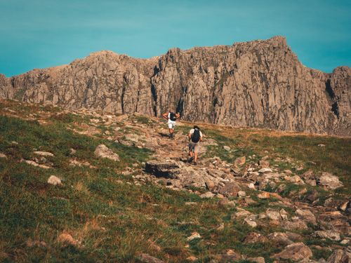Free Two hikers exploring a rugged mountain trail under clear skies, capturing a sense of adventure. Stock Photo