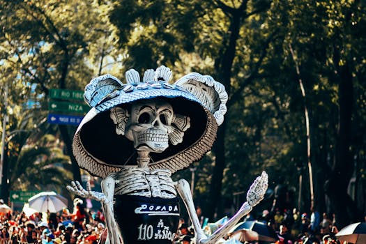 A colorful Day of the Dead parade with a giant skeleton sculpture in a lively city street.
