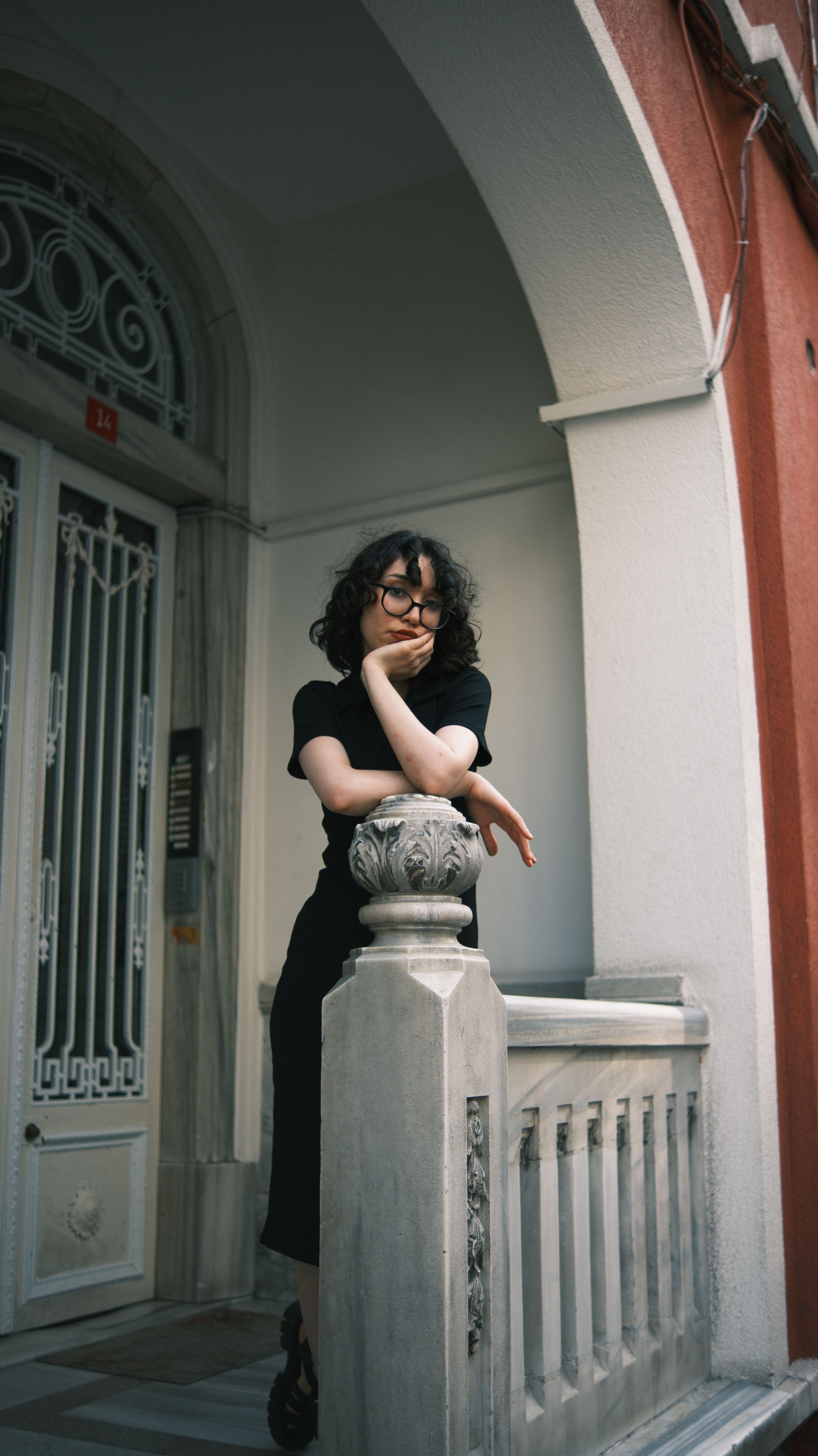Woman in black dress posing outdoors by a decorative entrance, exuding style and elegance.