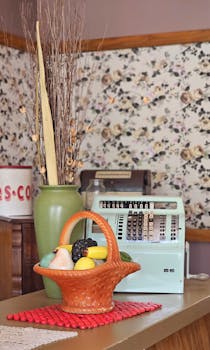 A nostalgic still life featuring a vintage cash register and decorative basket on a floral backdrop.