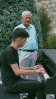 A man playing a piano outdoors with an observer in Baku, Azerbaijan. Musical moment captured.