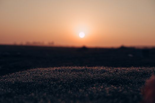 A serene close-up of dew on grass with a beautiful sunset in the background.