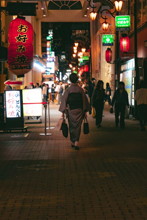 Woman in a Kimono Walking among Other Pedestrians on a Street in City at Night 