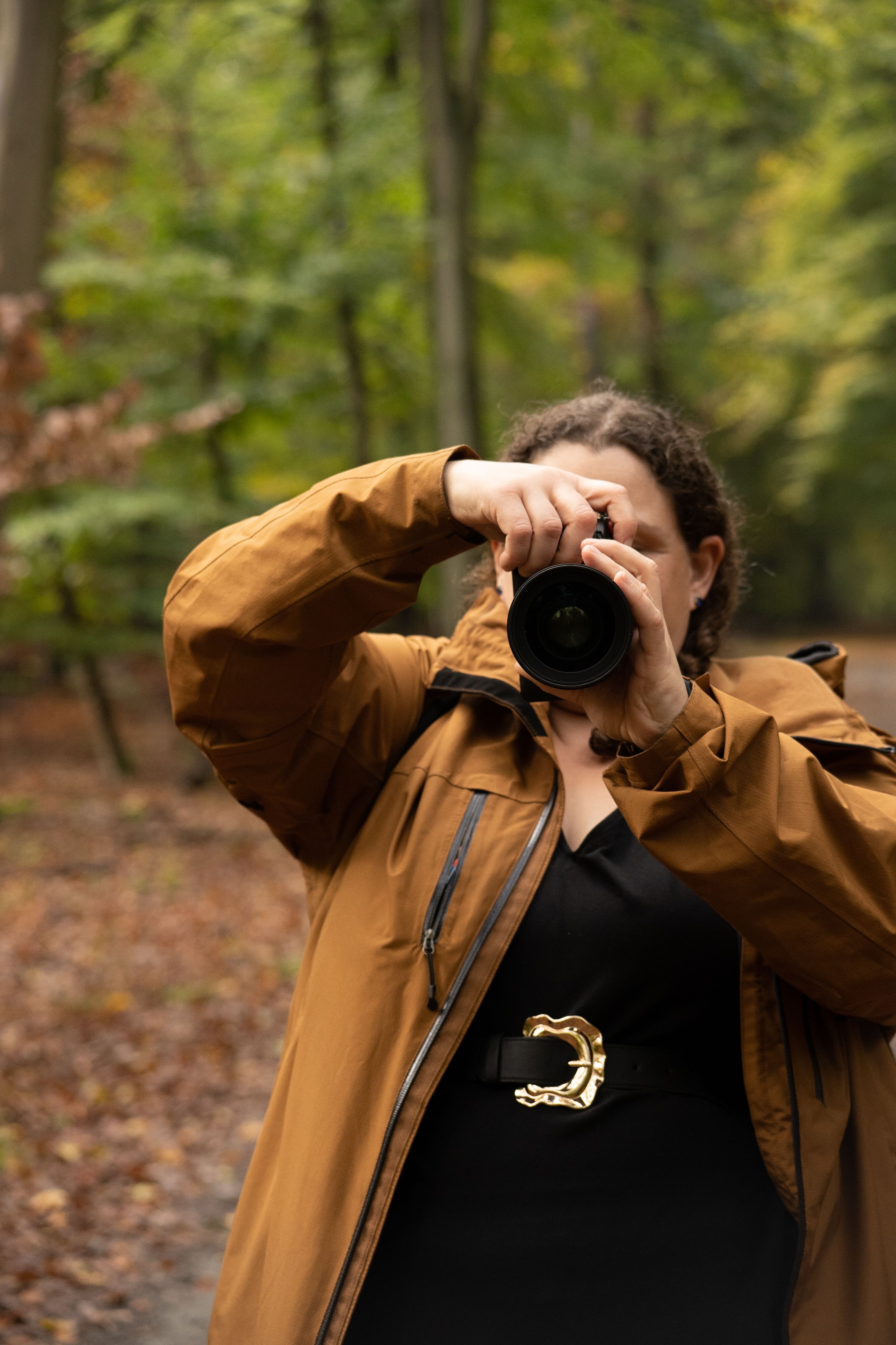 A woman in a brown jacket taking photos in an autumn forest.