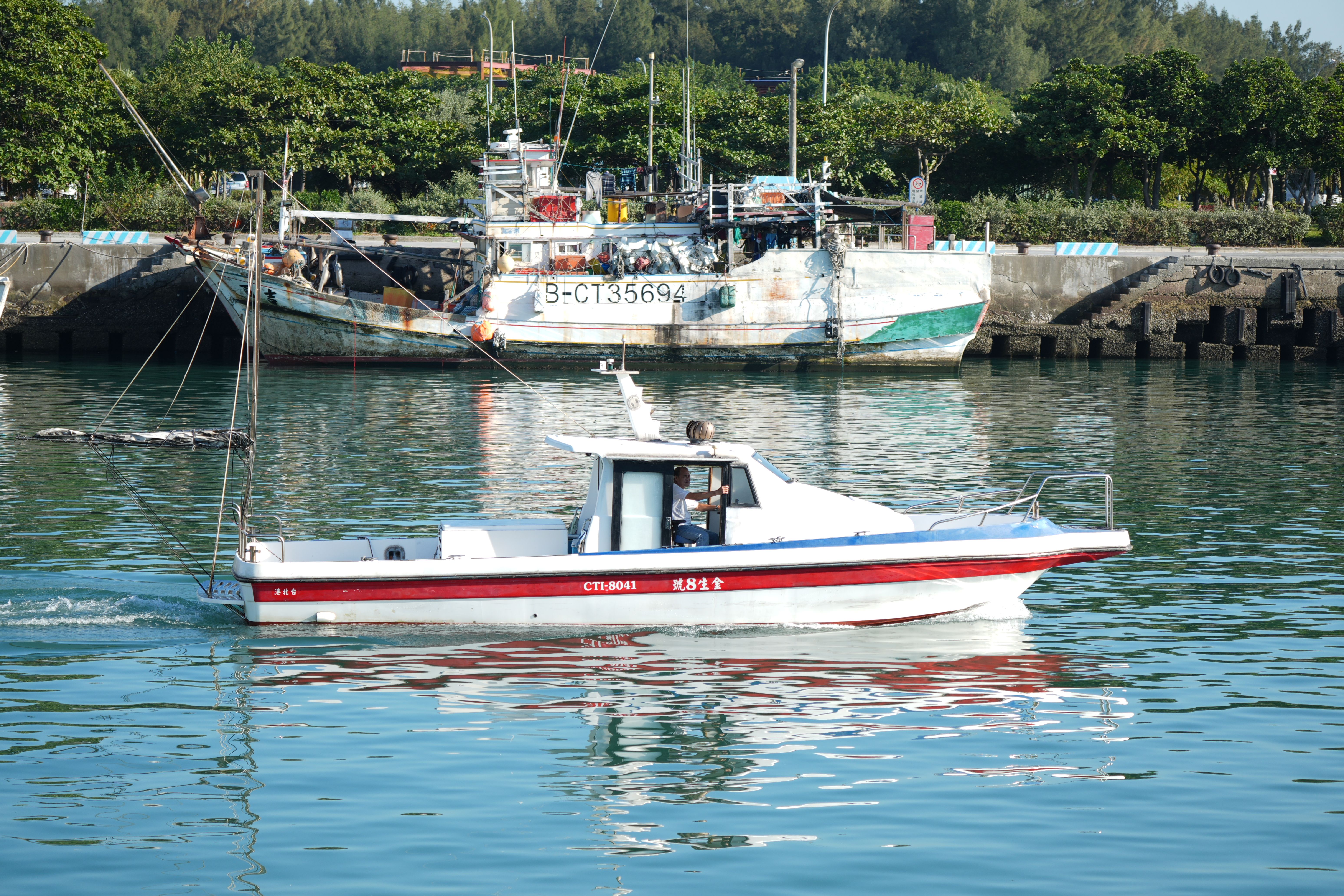 Motorboat cruising past moored fishing boats in a harbor.