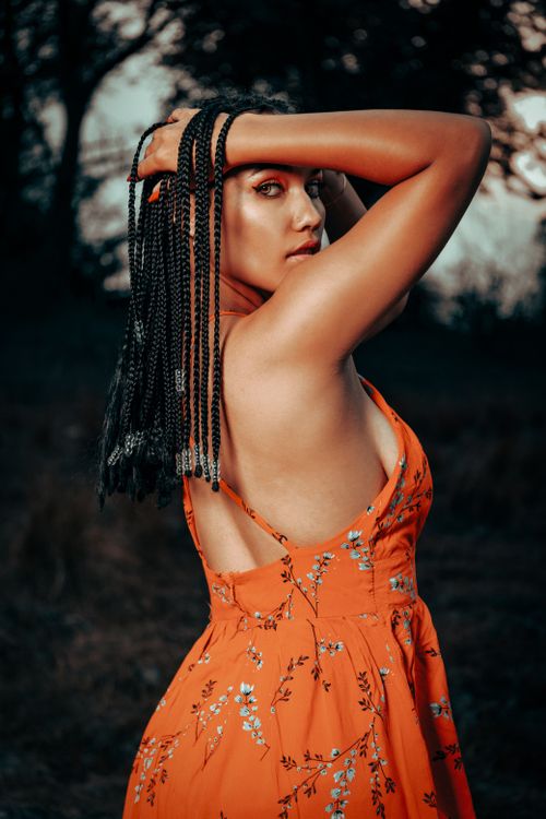 Free A woman with braided hair poses outdoors in a vibrant summer dress, exuding elegance. Stock Photo