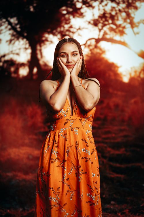 Free A young woman in an orange floral dress poses outdoors at sunset. Stock Photo