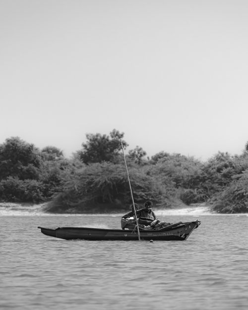 Free A lone fisherman in a canoe on a calm body of water framed by lush trees. Stock Photo